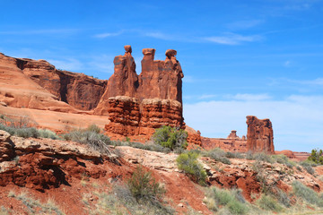 Naklejka premium Visiting Utah. Spring break travel concept.Amazing Utah landscape with road between red sandstones in Arches National Park, Moab, Utah, USA. Nature red sandstone sculptures and sparse green bushes.