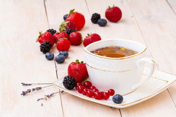 Herbal tea with lavender and mint, fresh strawberries, blackberries and blueberries on a white wooden table. Berry tea with fresh strawberry, blackberry.