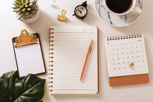 Flat lay desk with notebook, coffee, calendar and green leaf