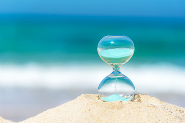 Hourglass summer and vacations time on a beach in the sand  with blue sky and copy space.  Lifestyle Concept..