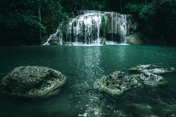 view of a beautiful waterfall in Thailand in a green jungle and clean environment in a moody green tone look surrounded with big trees and clear fresh green water which suggests an eco environment