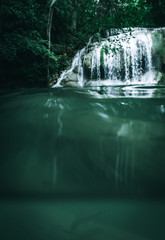 A waterfall taken from below the water with a fish in the foreground and the waterfall in the background within a beautiful jungle in Thailand in Asia in a healthy natural environment