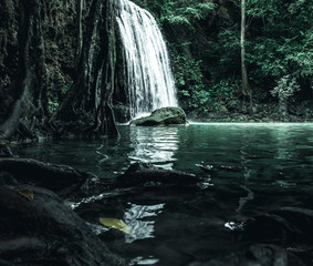 view of a beautiful waterfall in Thailand in a green jungle and clean environment in a moody green tone look surrounded with big trees and clear fresh green water which suggests an eco environment