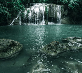 view of a beautiful waterfall in Thailand in a green jungle and clean environment in a moody green tone look surrounded with big trees and clear fresh green water which suggests an eco environment