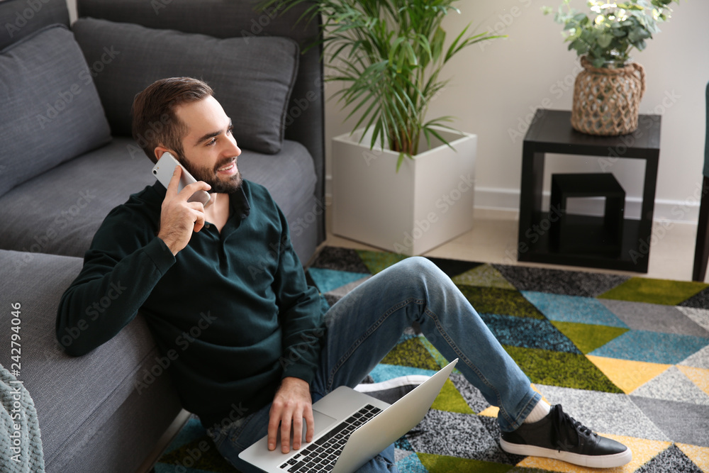 Wall mural Young freelancer talking on mobile phone while working on laptop at home