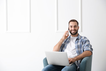 Young freelancer talking on mobile phone while working on laptop at home
