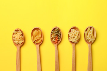 Spoons with assortment of uncooked pasta on color background