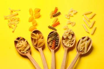 Spoons with assortment of uncooked pasta on color background