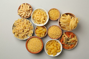 Bowls with assortment of uncooked pasta on grey background