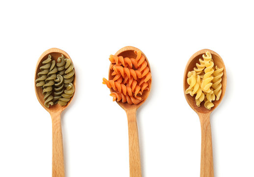 Spoons with uncooked fusilli pasta on white background