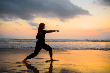 Fototapeta na wymiar silhouette of young fit Muslim woman covered in Islam hijab head scarf training martial arts karate punch attack and fitness workout at beautiful beach sunset
