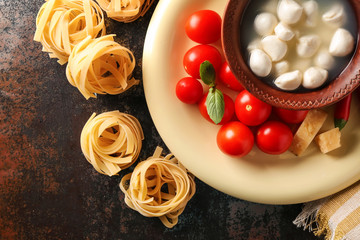Uncooked noodles with fresh products on dark table