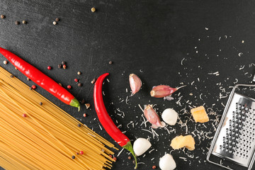 Uncooked spaghetti pasta with grater and fresh products on dark background