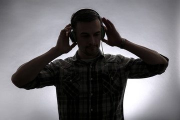 Silhouette of young man listening to music on grey background