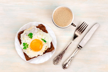 A plate with a sunny side up fried egg on a bread toast with coffee, a fork, and a knife, shot from above with a place for text