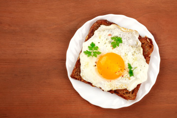 A sunny side up fried egg on a bread toast, shot from above on a dark rustic wooden background with a place for text