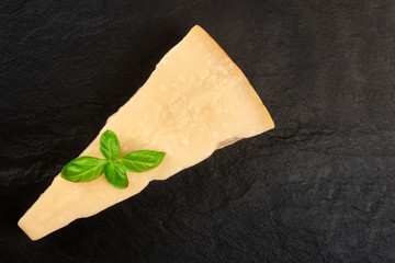 Aged Parmesan cheese, shot from above on a black background with fresh basil leaves and copy space