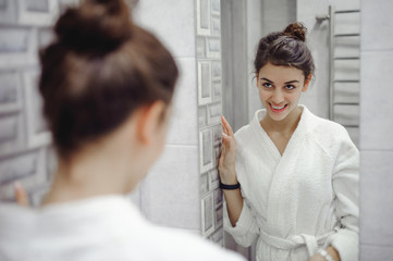 portrait of a beautiful woman in the bathroom. cheerful young girl looks at herself in the mirror,...