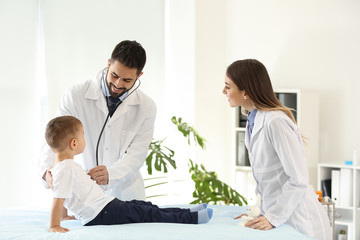 Male doctor with his colleague working with cute little boy in clinic