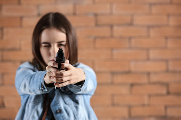young woman pointing a gun at viewer against brick background