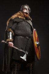 Warrior Viking in full arms with axe, shield and helmet on dark background