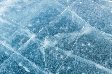 Texture of pure ice with cracks covered with small fresh snowflakes  on frozen river. Cold winter background.