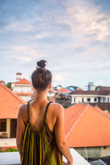 Fototapeta na wymiar Beautiful young woman sitting on a mountain, back view. Below - the sea and the tiled roofs