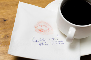 Napkin with a kiss and coffee cup on wooden background.
