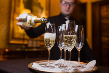 Waiter pouring champagne into glasses on a tray