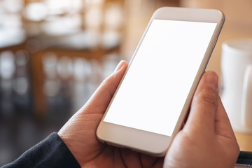 Mockup image of hands holding and using a white mobile phone with blank screen in cafe