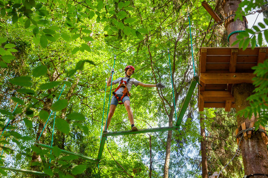 Teen boy on a ropes course in a treetop adventure park passing hanging rope obstacle