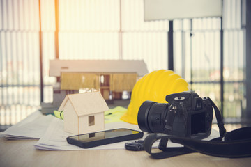 Selective focus of camera with  helmet Construction plans ,pem ,phone and blueprints on wooden table with sunshine background.