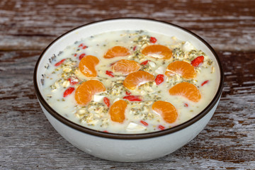 Fresh breakfast of granola, yogurt, nuts, goji berries, chia seeds and mandarin. Muesli with fruits and berries in bowl on a wooden background