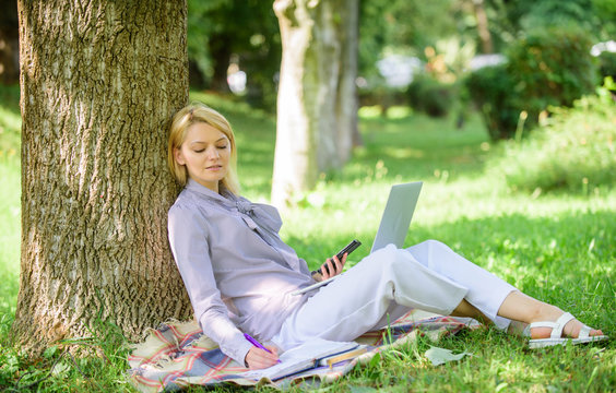 Woman with laptop computer work outdoors lean on tree trunk. Girl work with laptop in park sit on grass. Natural environment office. Work outdoors benefits. Education technology and internet concept
