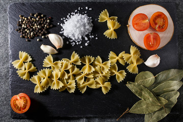 Whole grain raw Italian pasta and ingredients composition on black rustic slate stone background, top view with copy space