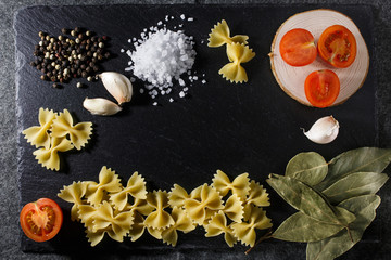 Whole grain raw Italian pasta and ingredients composition on black rustic slate stone background, top view with copy space