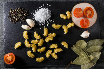 Obraz na płótnie Canvas Whole grain raw Italian pasta and ingredients composition on black rustic slate stone background, top view with copy space