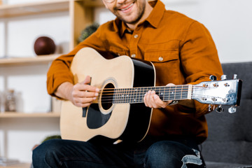 cropped view of cheerful man playing acoustic guitar