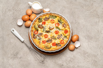 Baked homemade quiche pie in ceramic baking form, eggs and cream