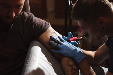 Tattoo artist makes a tattoo on a man's hand.