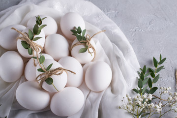 Easter concept. White chicken eggs on white fabric. Decorated with eucalyptus leaves. Top view and copy space.