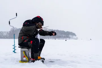 Fototapeten Winter fishing. Ice fisherman fishing on the lake in the cold winther day © smspsy