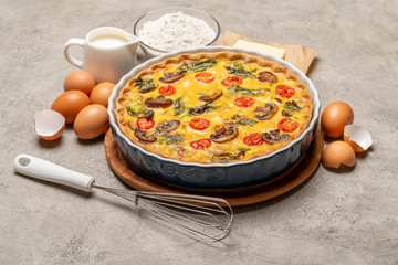 Baked homemade quiche pie in ceramic baking form, eggs and cream
