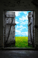 Open wood door in abandoned house. Green sunny meadow outside.