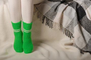 Female legs in warm white knitted tights and green socks on a white background made of faux fur