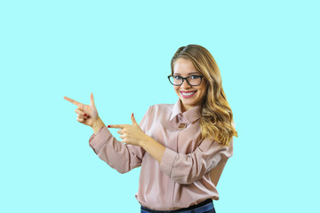 Attractive blonde girl in shirt and glasses stands sideways with a smile and points fingers at copyspace