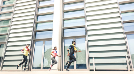 Young people running in modern urban area - Fitness girls running with male trainer coach in the city - Sport concept with friends group jogging in business center downtown on sunny day bright filter