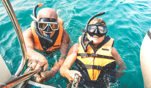 Retired couple taking happy selfie in tropical sea excursion with life vests and snorkel masks - Boat trip snorkeling in exotic scenarios on active elderly and senior travel concept around world