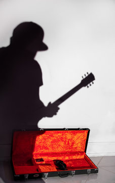 Guitarist in a baseball cap and his shadow on the background of the guitar case