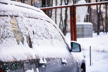 Snow covered ows of cars in the parking lot. Urban scene, snowstorm. Clean automobile from the snow.